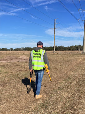 Surveyor with safety vest and locator device identifying underground utilities in open field in Sunrise by Land Roadway Solutions